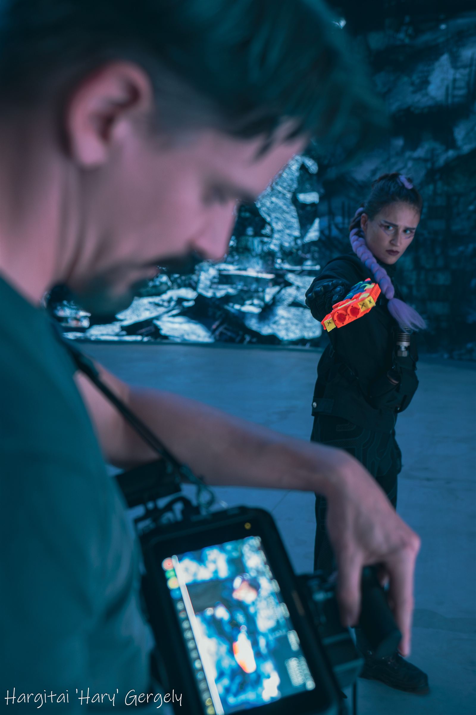 Actress in black tactical costume aiming a prop weapon toward the camera operator